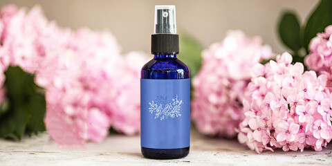 A blue spray bottle sits among pink flowers, suggesting a soothing or fragrant product, ideal for beauty or relaxation.