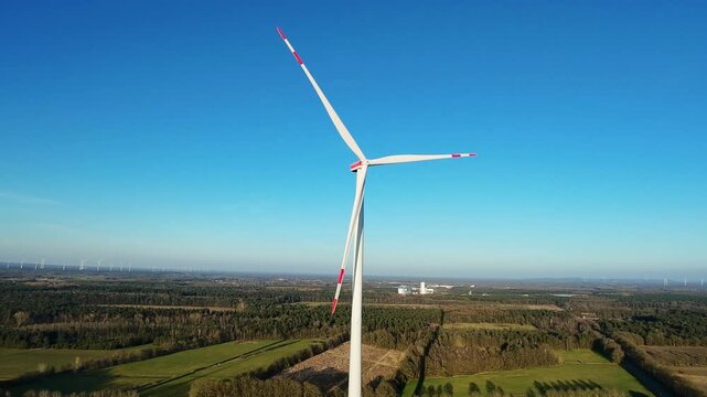 Distant View Of Solitary Turbine Over Farmland With Scattered Distant Turbines, Clear Blue Sky And Rolling Fields Suggest Sustainable Future Planning By Energy Developer Surveying Landscape