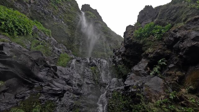 Water cascades down steep basalt cliffs at Cascata do Poco do Bacalhau, a dramatic waterfall near Faja Grande on Flores Island, Azores, Portugal