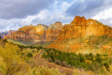 A winding road curves through a broad canyon framed by towering sandstone cliffs in Zion National Park, Utah.