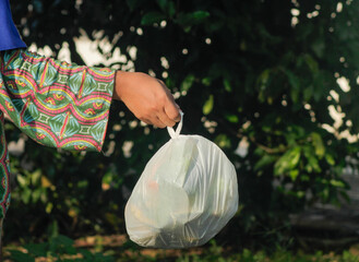 Hand holding a full black plastic trash in outdoor	