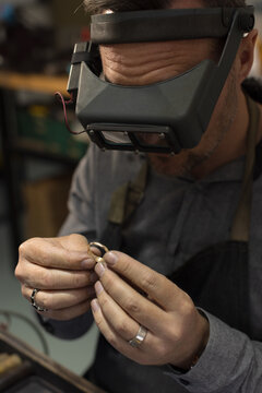 A jeweller wearing goggles and focusing on a ring in his hands