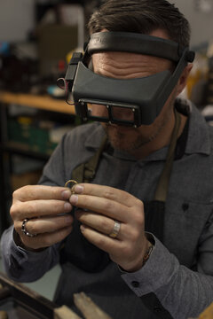A jeweller wearing goggles and focusing on a ring in his hands