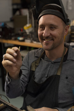 A jeweller smiling at a ring he is holding in his hands