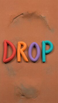 Colorful clay letters spelling 'DROP' on a brown background with smudges
