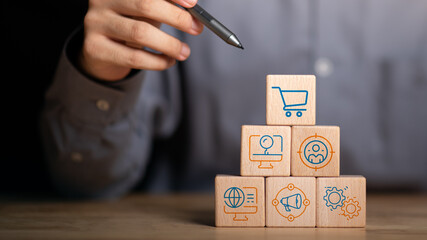 Stacked wooden cubes with digital marketing icons such as shopping cart, SEO, analytics, audience targeting, and automation, representing strategic marketing structure and planning.
