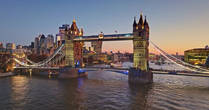 Iconic Tower Bridge illuminated against beautiful twilight sky, reflecting in River Thames, with vibrant London city skyline visible in the background. Urban cityscape panorama at evening sunset glow