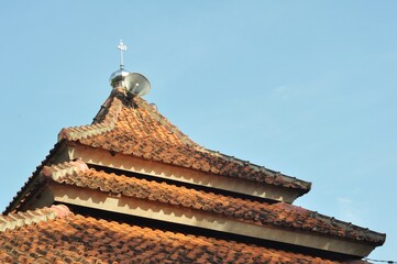 Traditional Indonesian Mosque Roof with Loudspeaker and Blue Sky