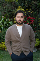 Serious young man with arms crossed in lush garden, confident outdoor portrait