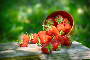 A bowl of fresh, ripe strawberries spills onto a wooden table.