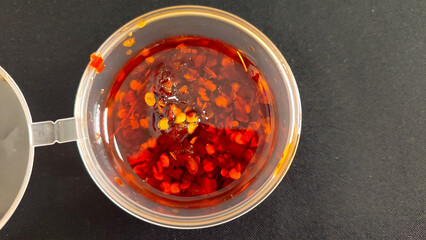 Close-up of spicy chili oil with red pepper flakes in a clear plastic container. Hot chili sauce...