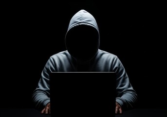 Person in hoodie using laptop in dark room with shadows conveying secrecy and anonymity