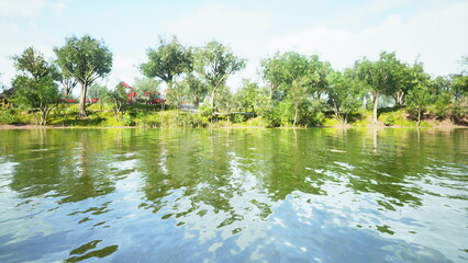 Obraz premium Bright sunlight dances on tranquil waters surrounded by green trees. The peaceful riverbank offers a picturesque view of natures beauty, inviting relaxation and reflection.