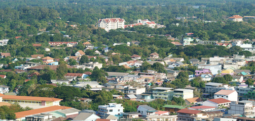 high angle view of a suburban town in Thailand featuring a mix of residential houses, modern buildings, and lush green tropical vegetation under bright daylight. Scenic urban landscape.