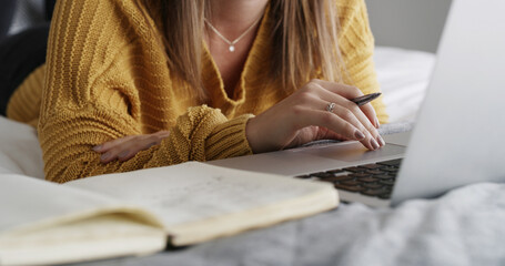 Hands, laptop and book for student on bed, home and online course with notes, study and scholarship. Person, computer and scroll with assessment, elearning and education with virtual college project