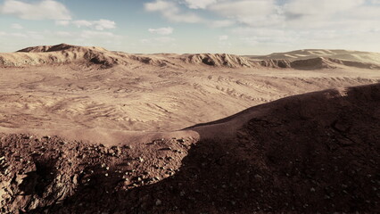 A vast desert stretches under a clear blue sky, showcasing undulating hills and textured earth. Shadows dance on the rocky surface, creating a dramatic view in a remote location.