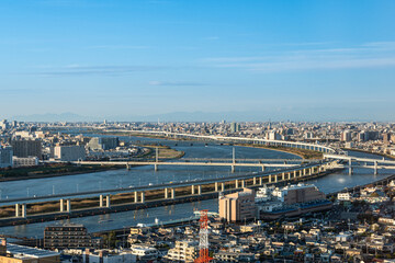 An elevated view of Tokyo's sprawling cityscape, with the wide Arakawa River and its multiple bridges cutting through the urban landscape.