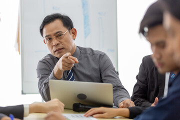 Serious businessman in formal attire pointing during tense meeting, expressing authority, leadership at office conference table with colleagues. Ideal for concepts decision making.