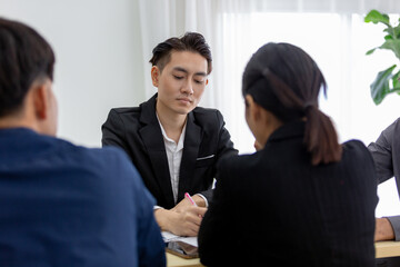 Asian businessman in black suit listening carefully in a business meeting, demonstrating attention, professionalism, collaboration. Ideal for concepts of teamwork, planning and business strategy.