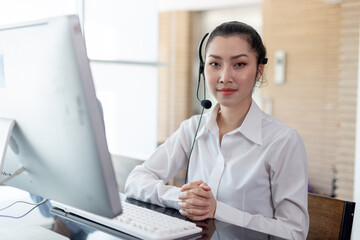 Asian female call center agent wearing headset and sitting at computer, ready to assist with customer service or online communication. Ideal for support, contact center, virtual assistant themes.