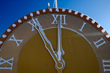 Vintage red clock with Roman numerals showing midday time close-up