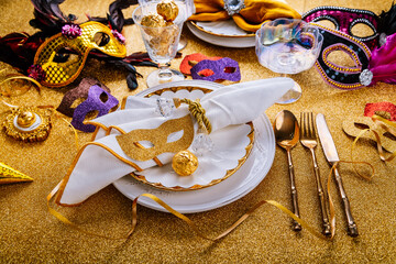 Festive place setting for carnival, party with masks, confetti and golden pralines