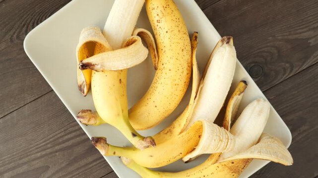 Fresh organic bananas rotating on a white plate on a wooden table, top-down view.