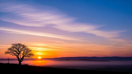 Sunrise silhouettes a bare tree and cross against a misty landscape under a colorful streaked sky