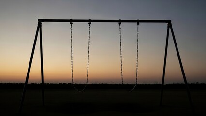 A silhouetted swing set with four swings stands against a muted sunset sky