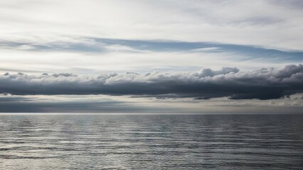 A tranquil scene shows the ocean under a cloudy sky with serene horizontal waves and varying cloud layers