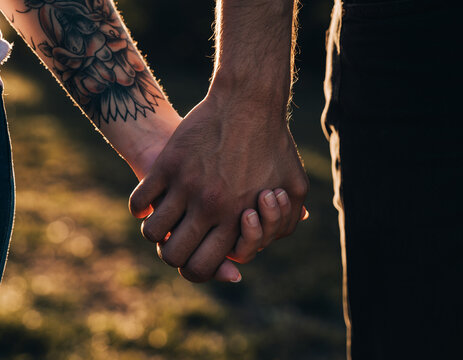 Non-Binary Couple Hand Holding. Valentine&rsquo;s Day - Modern Romance. Close-up of two hands one with unique tattoos holding gently representing a non-binary couple's connection. Focus on unique details..
