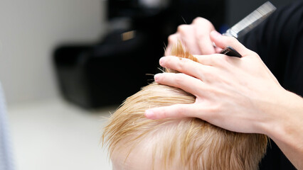 Fototapeta premium Hairdresser cutting boy's blond hair in barbershop