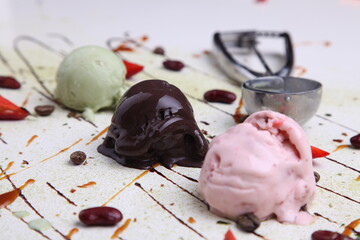Three scoops of ice cream chocolate strawberry and pistachio with sauce drizzle and berries on...