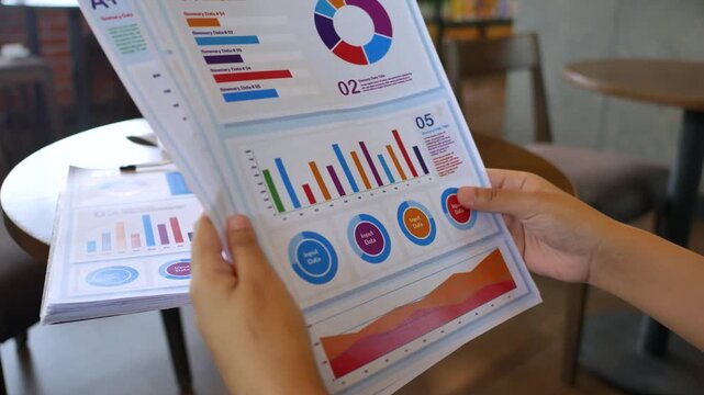 An entrepreneur studies printed infographic charts and business summaries at a caf&eacute;, combining data analysis with a relaxed environment to support planning, productivity, and smart decision-making.