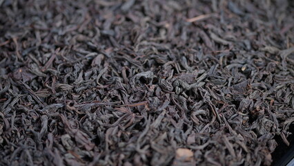Closeup dried black tea on tray, industrial quality control context, fine wiry leaves, muted brown palette, commercial batch texture, methodical composition, supply chain theme