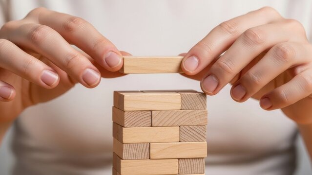 Hands carefully placing final wooden block on tower game, symbolizing strategy, focus, risk management, teamwork and building strong foundations for success

