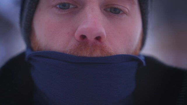 Man adjusting jacket zipper and neck gaiter outdoors