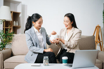 Businesswomen discussing financial planning and saving money using piggy bank at home office. Investment, budget, teamwork, female leadership