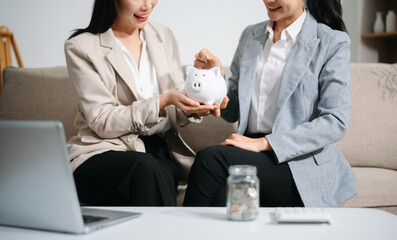 Businesswomen discussing financial planning and saving money using piggy bank at home office. Investment, budget, teamwork, female leadership