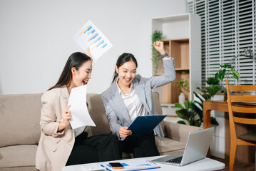 Happy Asian businesswomen celebrating success together at office. Teamwork, collaboration, business achievement, financial growth and positive corporate work concept.