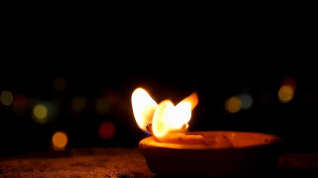 Flame of a clay oil lamp flickering in the wind during a festival night