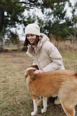 Fototapeta premium Woman in a warm winter coat and beanie outdoors, gently touching a friendly dog in a grassy field on a chilly day, capturing a candid moment of companionship and nature.