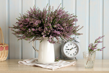 Still life composition with heather flowers and clock on table