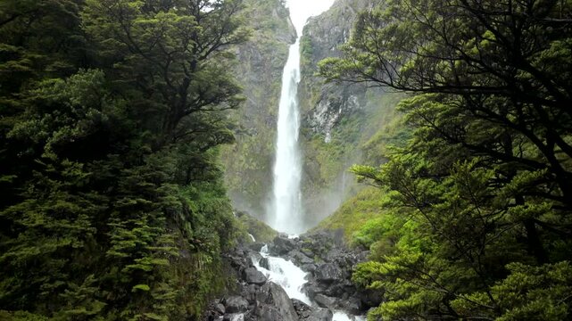 Slow tilt down high waterfall in lush green gorge