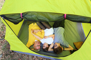 A father and two kids rest peacefully inside their yellow tent, lying side by side. A quiet, cozy moment of family closeness and calm on a camping trip.