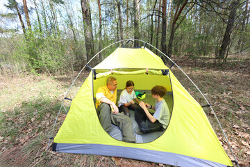 A father and two kids relax inside their bright yellow tent in a sunlit forest. A cozy moment of connection, conversation, and shared adventure in natures embrace.