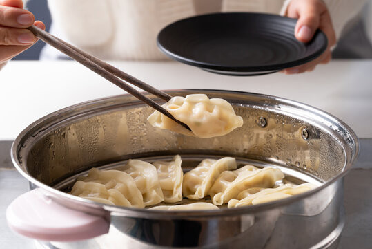 Hot steamed dumpling being picked up by chopsticks from a steamer pot to a black plate
