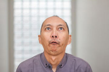 Fototapeta premium Portrait of an Asian man looking upward with a neutral thinking expression.