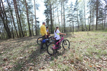 A father and two kids walk with bikes through a sun-dappled forest, heading toward adventure. A peaceful moment of family bonding and outdoor exploration in nature.