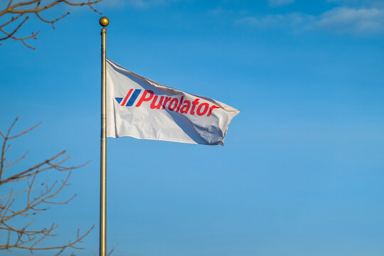 Calgary, Alberta, Canada. Jan 19, 2026. A white Purolator corporate flag waving on a flagpole against a clear blue sky.